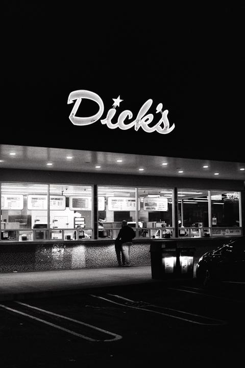 A man stands at a brightly lit Dick's restaurant counter at night.