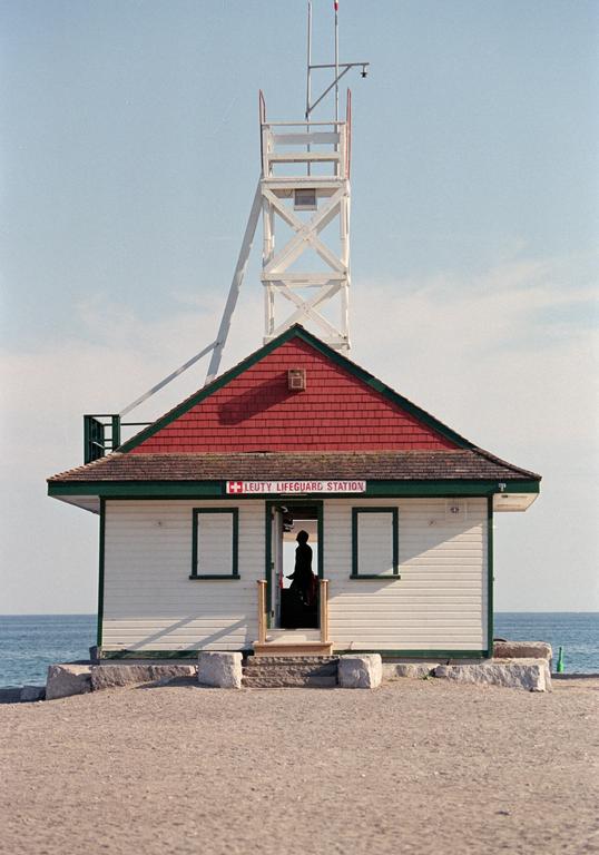 A lifeguard station with a tall tower stands on a sandy beach next to the ocean, with a person silhouetted in the doorway.