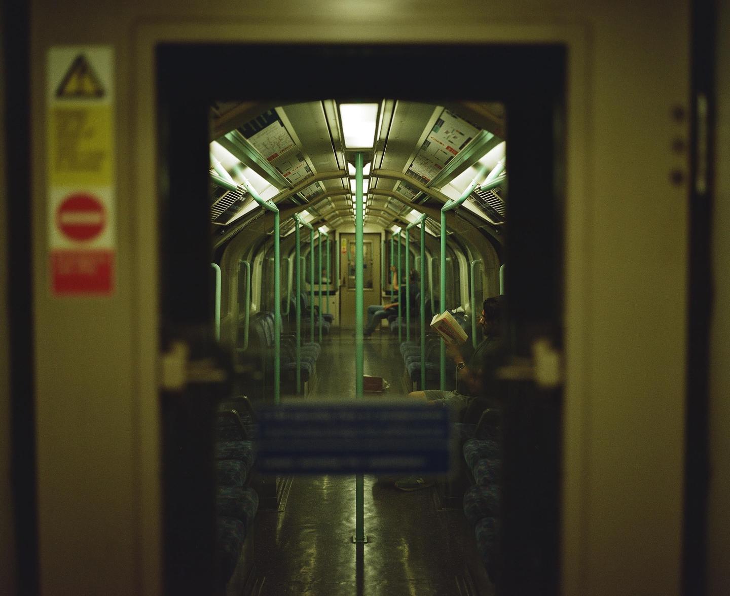 A person reads a book inside a subway car, viewed through an open doorway.