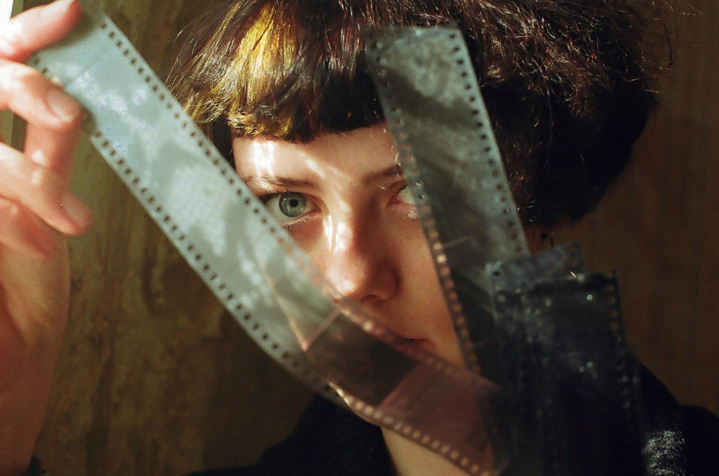 A woman with short hair looks through strips of film held in front of her face.