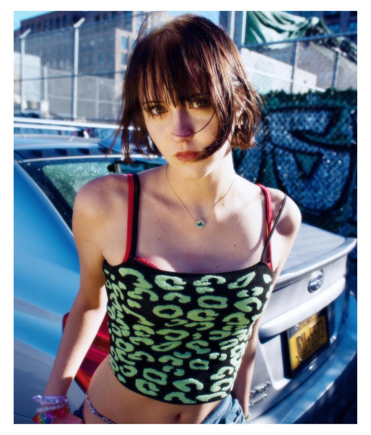A woman with short hair and a patterned top stands in front of a car.