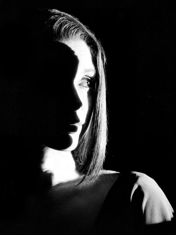 A woman's face is illuminated by a strong light from the side, casting half of her face in shadow.