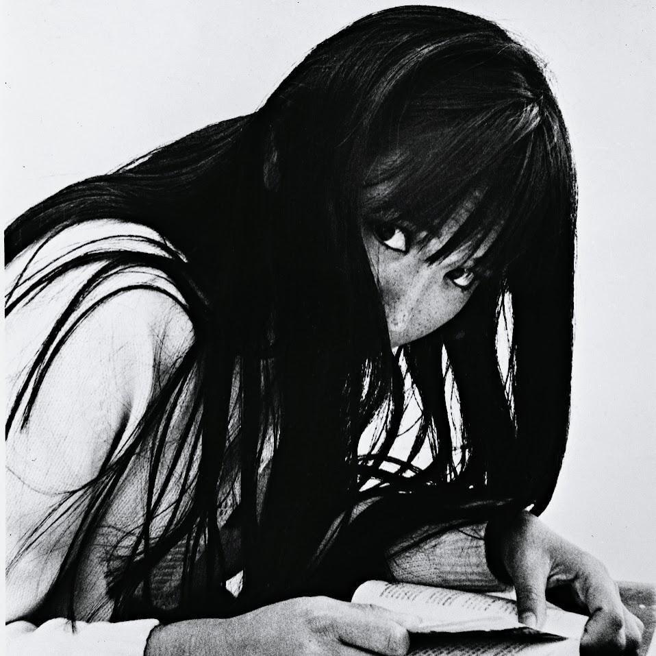 A woman with long dark hair looks up from a book she is reading.
