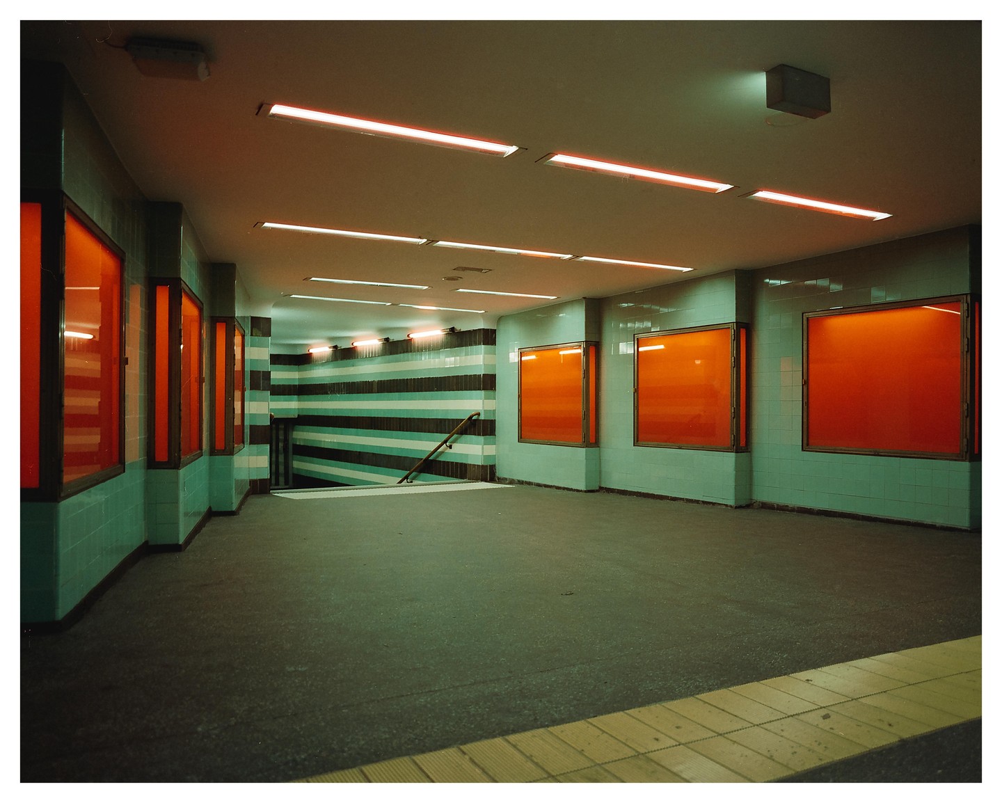 A brightly lit underground passageway features orange-red display cases and a striped wall leading to a staircase.
