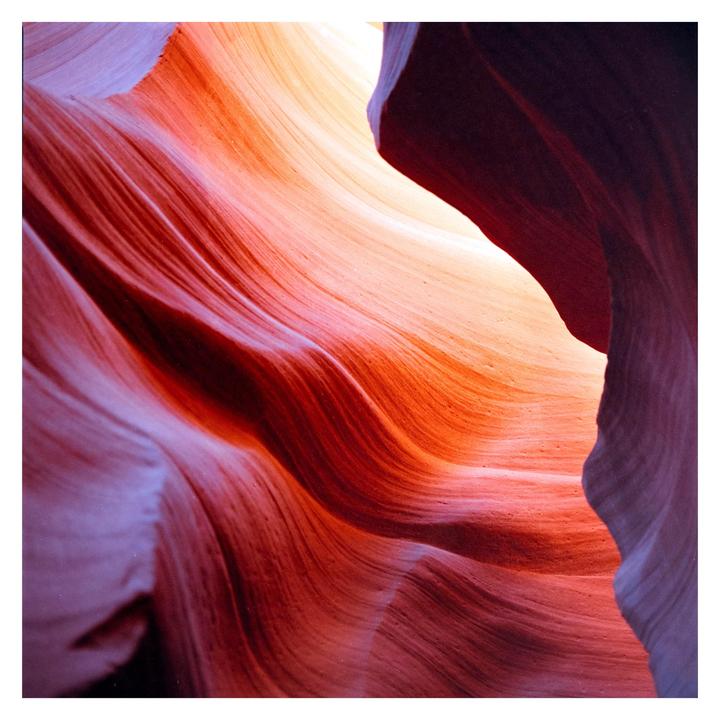 Light illuminates the wavy, colorful rock formations of a slot canyon.