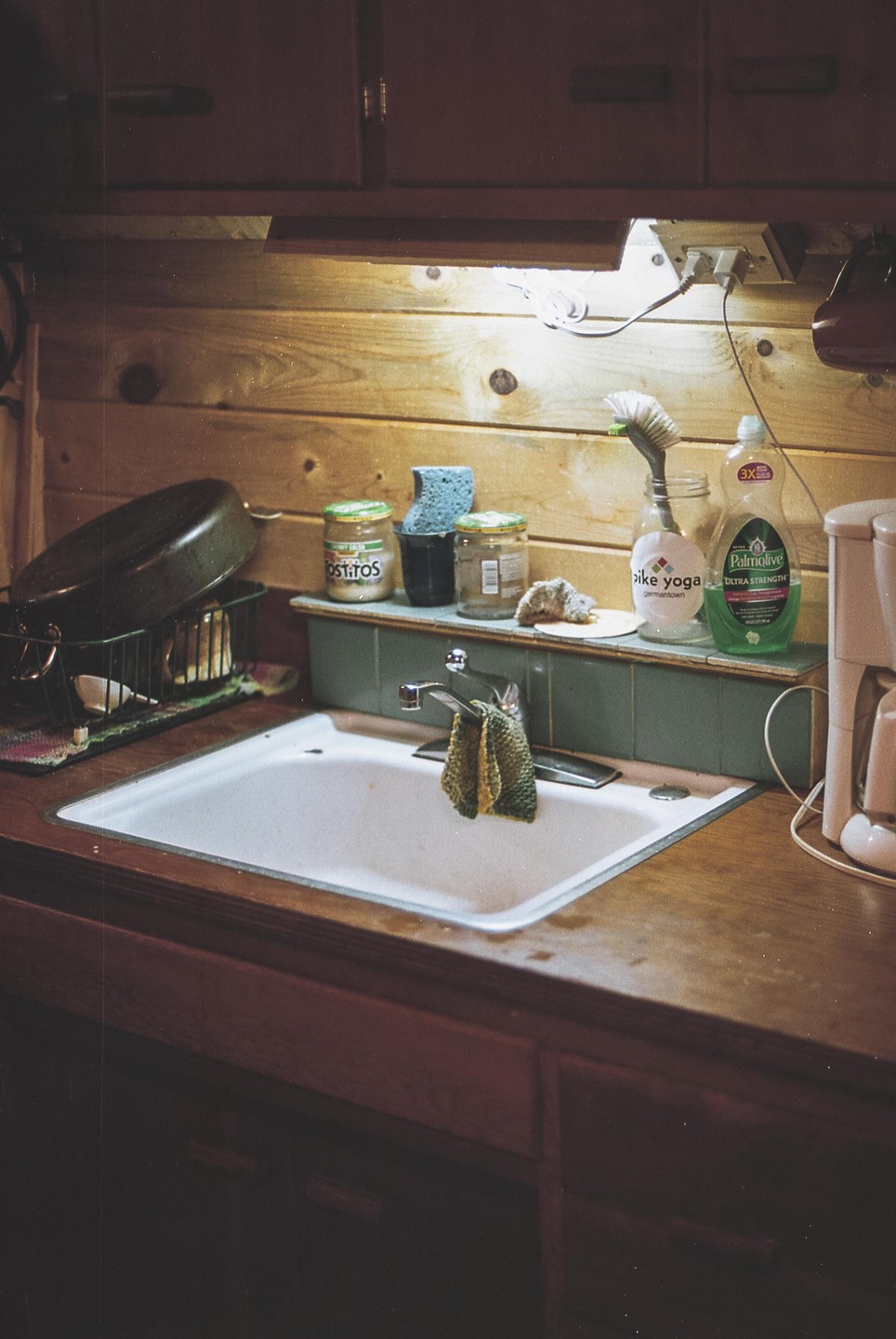 A kitchen sink is surrounded by various cleaning supplies and a dish drying rack with a pan.
