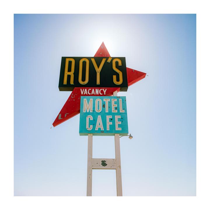 A vintage motel and cafe sign with a red star is visible against a bright sky.