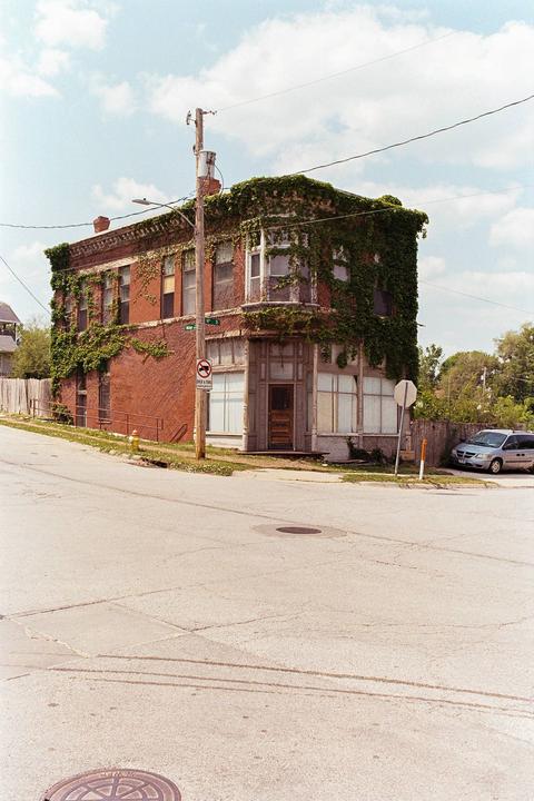 A brick building covered in ivy stands at a street corner under a partly cloudy sky.