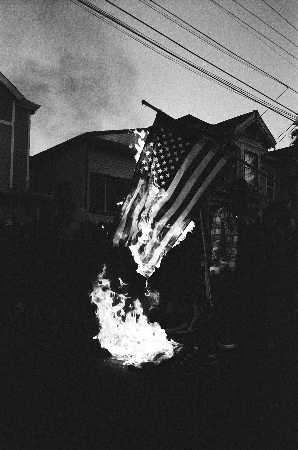 An American flag is burning in front of houses with power lines overhead.