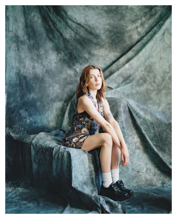 A woman with red hair sits on a draped surface in a studio.