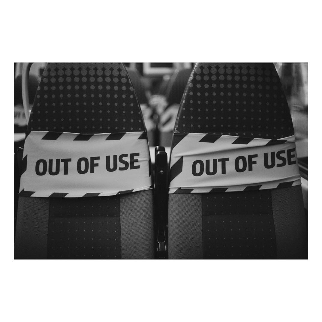 Two train seats are marked with "OUT OF USE" tape in a black and white photograph.