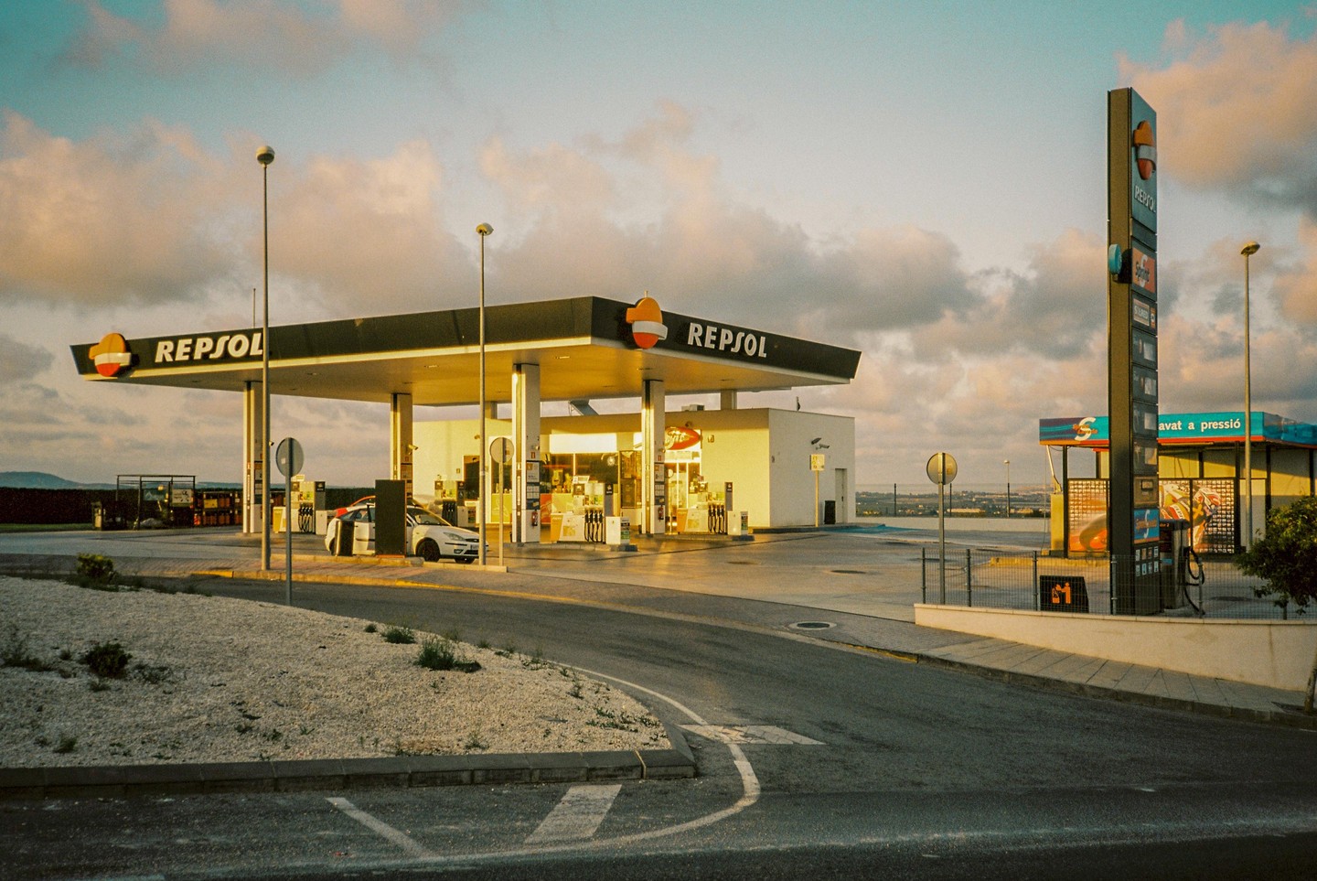 A Repsol petrol station is visible under a cloudy sky with a car parked at one of the pumps.