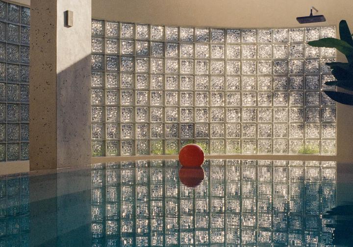 A red ball floats in a swimming pool next to a wall of glass blocks.
