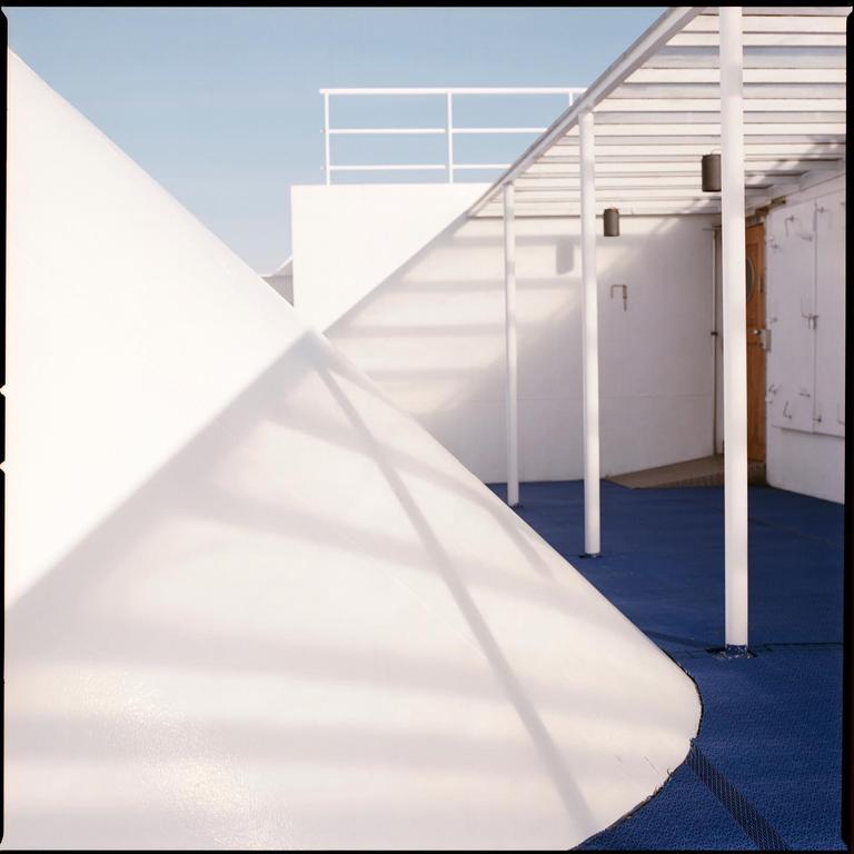 Sunlight casts shadows on the white structures and blue deck of a ferry.
