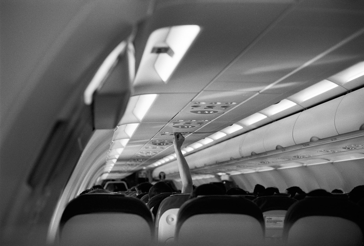 A person's arm reaches up to adjust an overhead vent inside an airplane cabin filled with passengers.