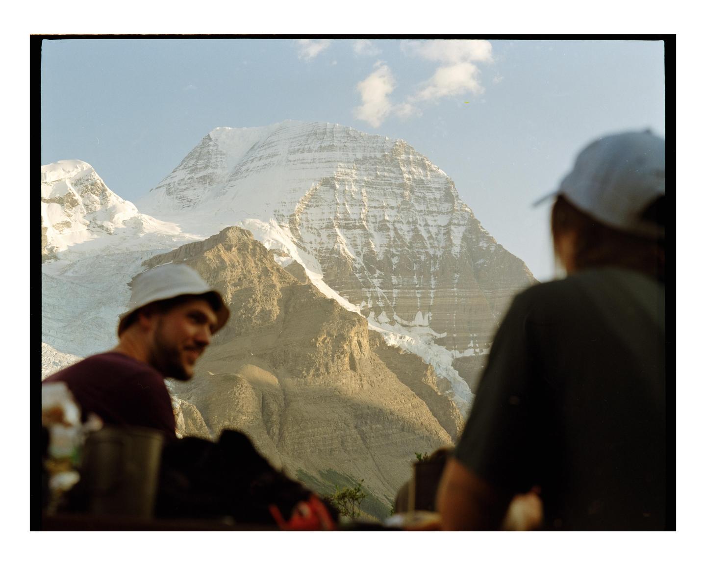 Two people are sitting with a view of a large, snow-capped mountain.