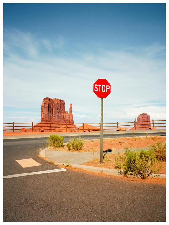 A stop sign stands at a desert intersection with large rock formations in the background.