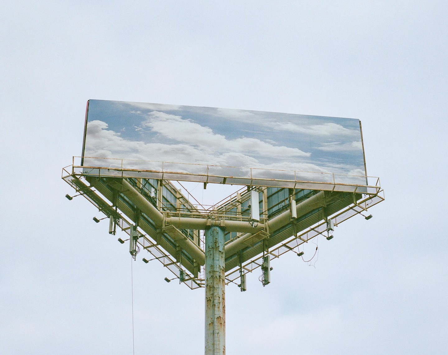 A billboard with a cloudy sky advertisement stands against a light sky.