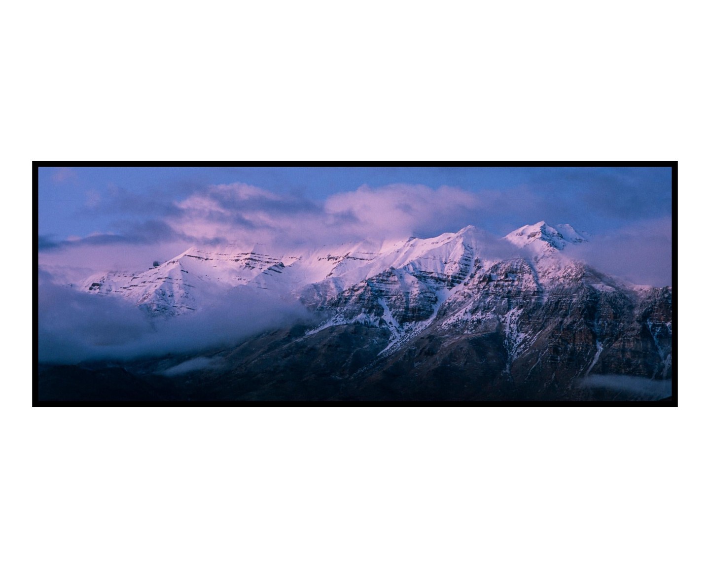 Snow-capped mountains are partially obscured by clouds under a purple sky.