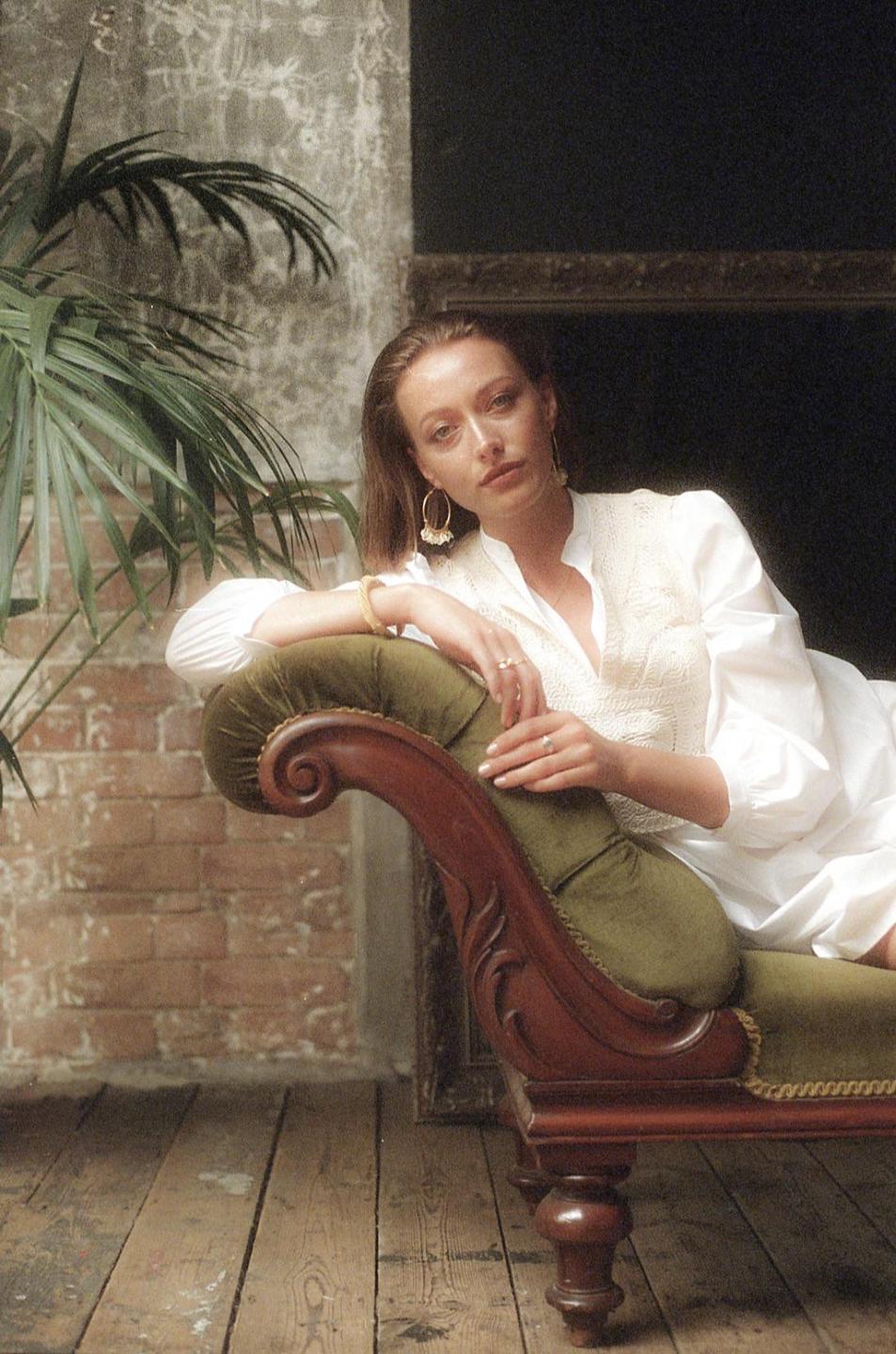 A woman in a white shirt reclines on a green chaise lounge next to a plant.
