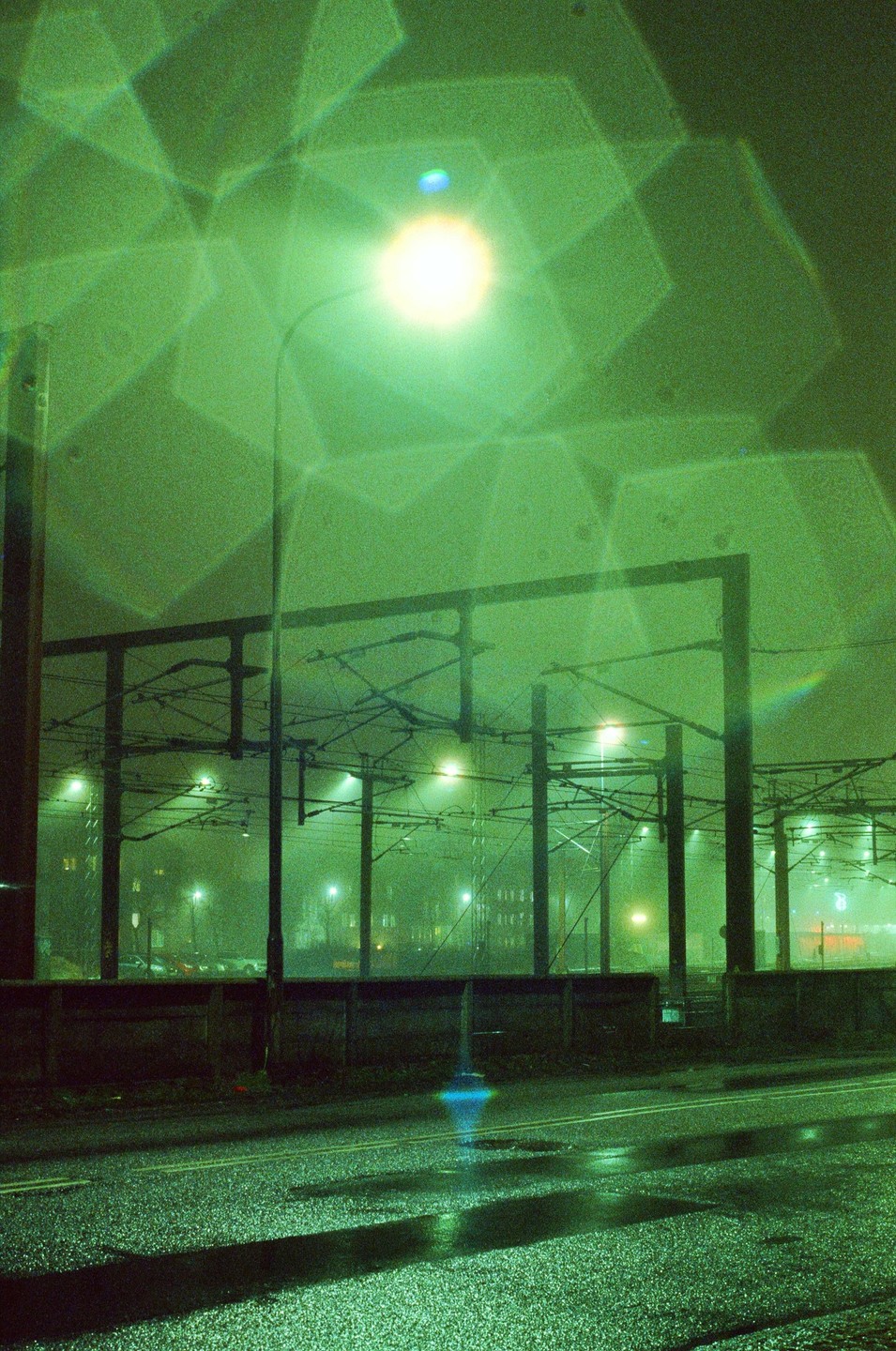 A street light illuminates a wet street and overhead power lines at night.