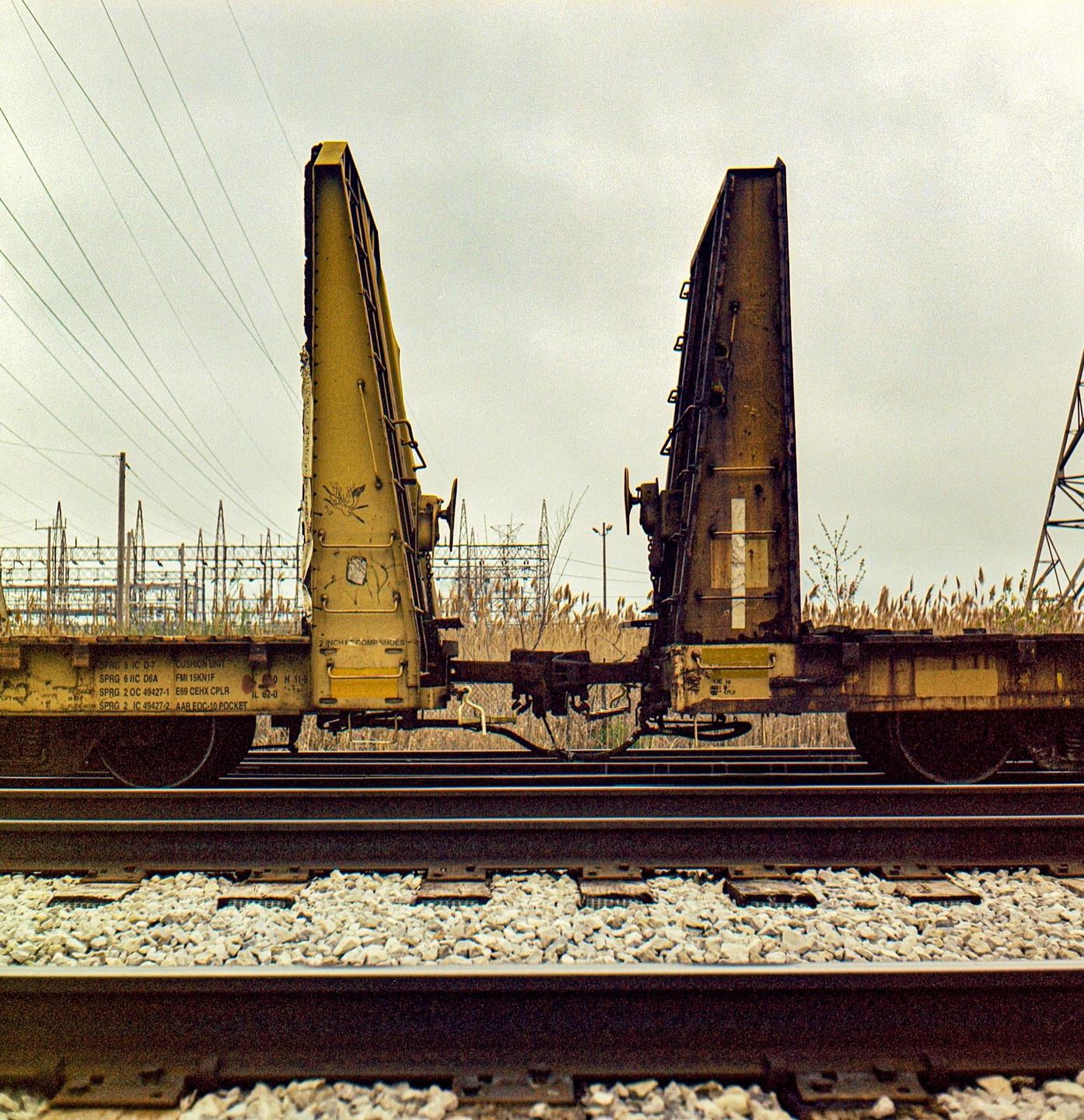 Two yellow train cars with large, upright structures are parked on railroad tracks under an overcast sky.