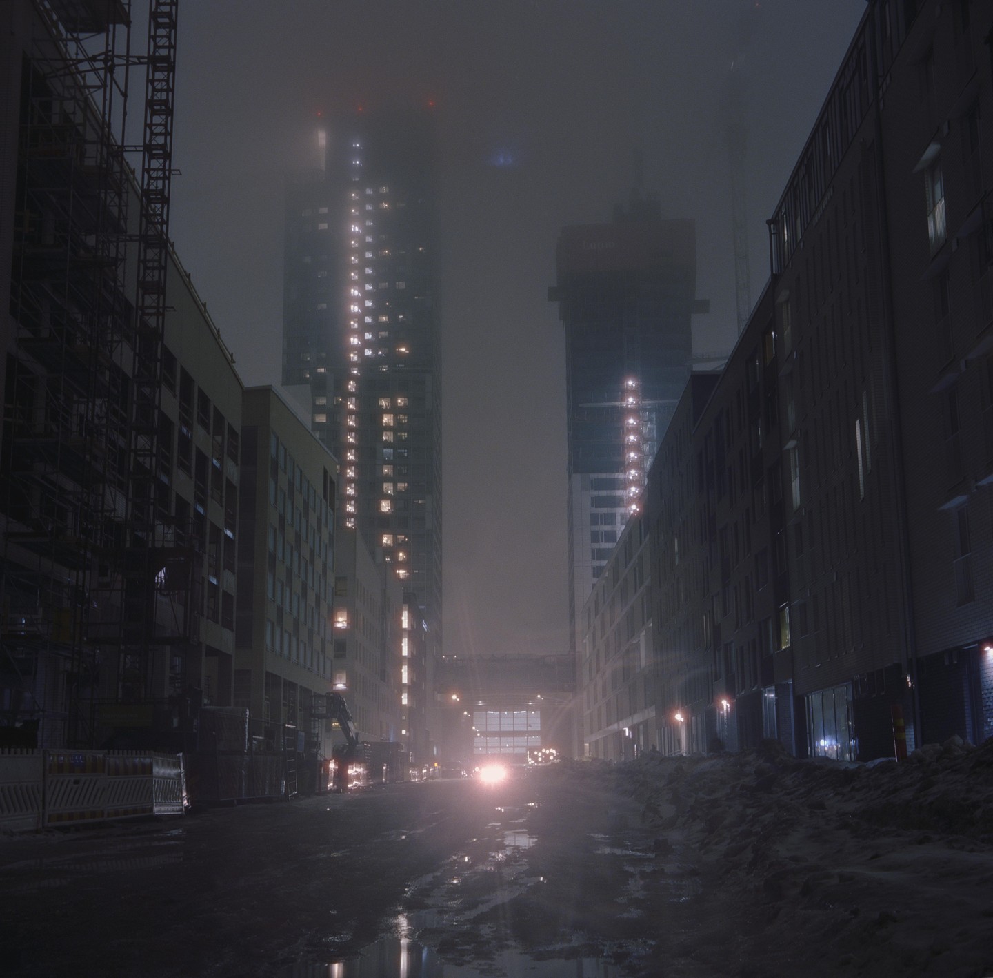 A street in Helsinki is covered in snow and slush, with tall buildings and construction sites visible through the fog.