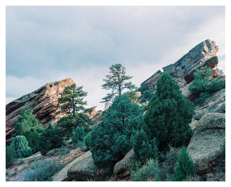 Large rock formations and evergreen trees are visible on a hillside under a cloudy sky.