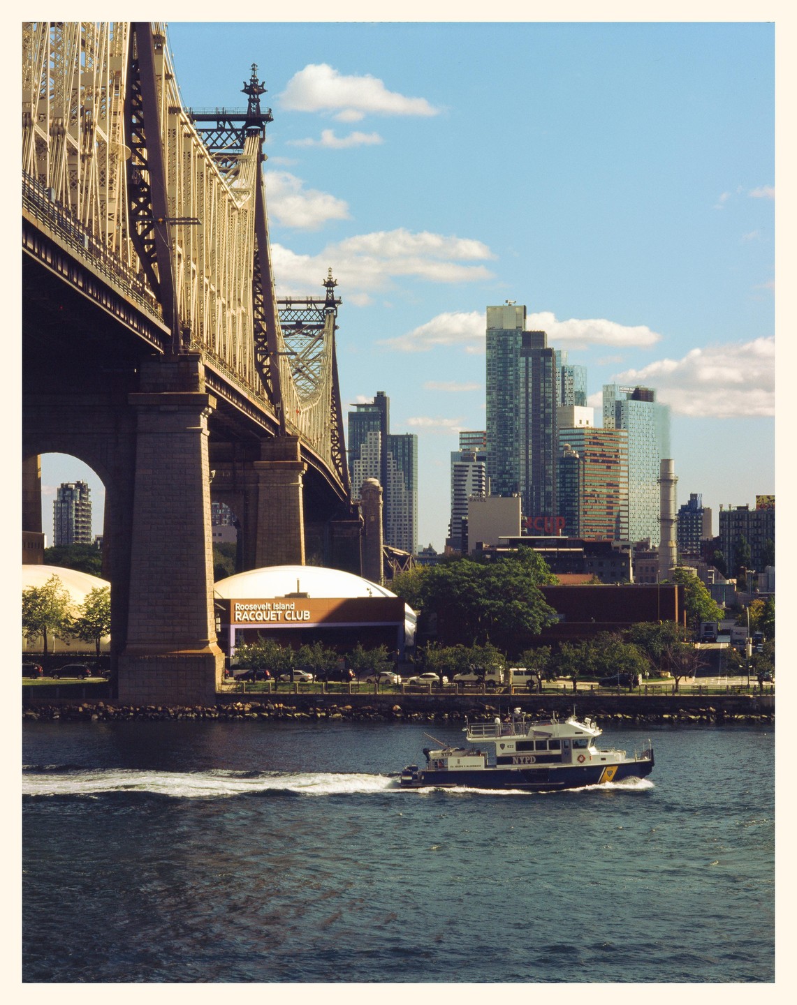 A boat travels on the East River with a bridge and city skyline in the background.