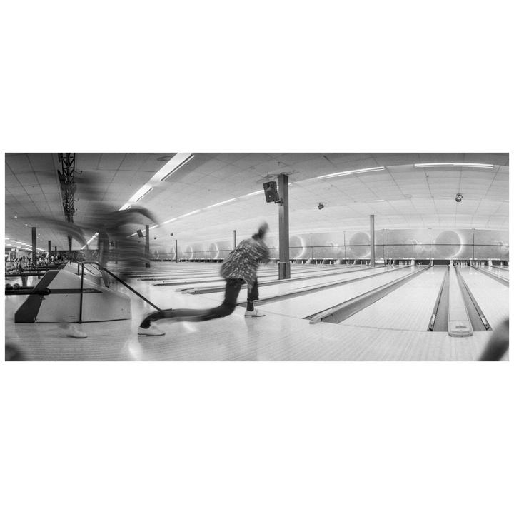 A person bowls in a bowling alley with motion blur.