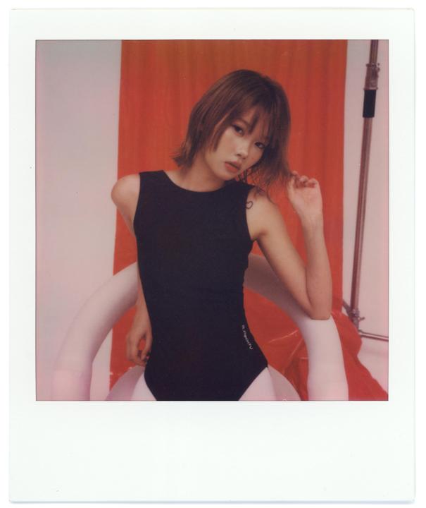 A woman in a black leotard poses in front of a red backdrop.