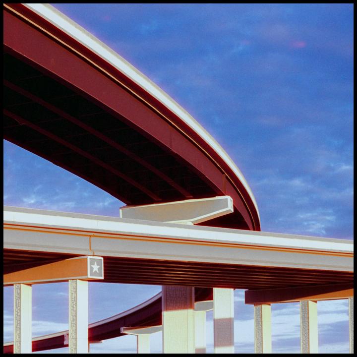 A complex highway interchange with multiple elevated roads is shown against a blue sky.