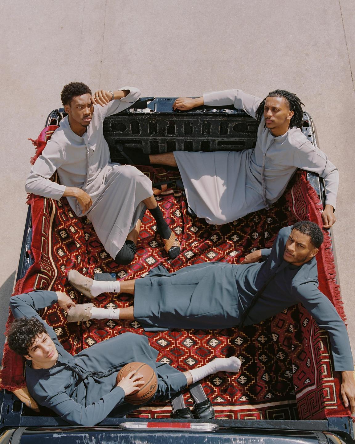 Four men are posing in the back of a pickup truck covered with a patterned rug.