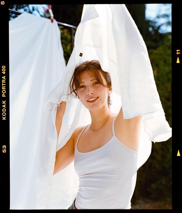 A woman smiles at the viewer while holding a white sheet over her head.