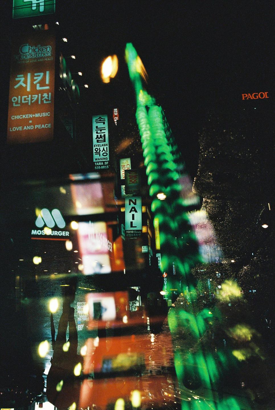 A street at night is illuminated by neon signs and reflections on a wet surface.