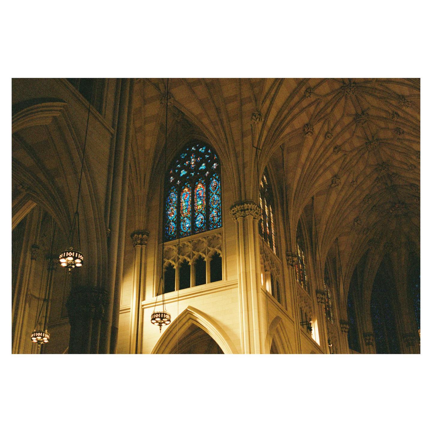 The interior of a cathedral features a large stained glass window and vaulted ceilings.