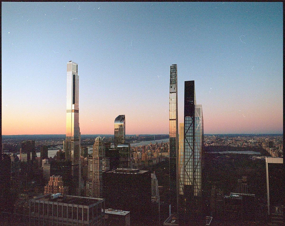 A cityscape with several tall skyscrapers reflecting the light of the setting sun.