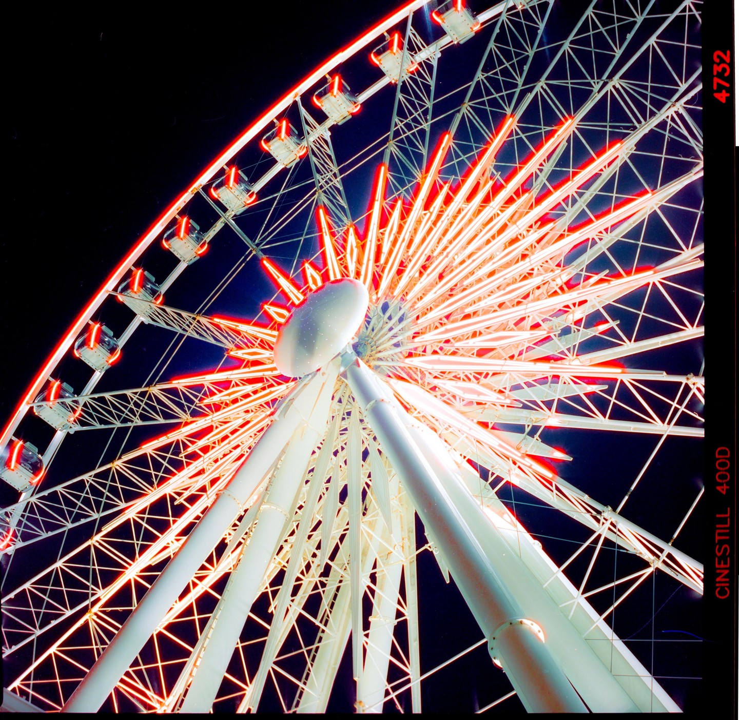 A low-angle view of a ferris wheel at night, illuminated with red and white lights.