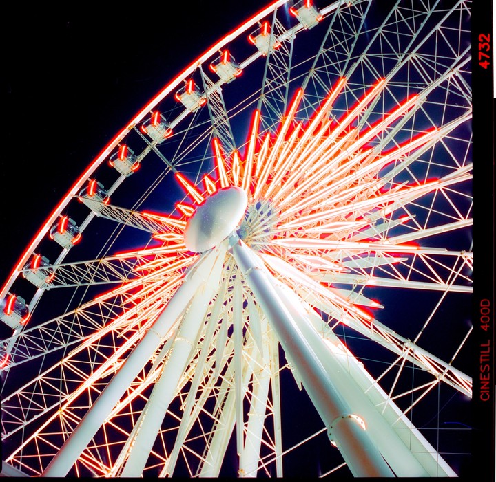 A low-angle view of a ferris wheel at night, illuminated with red and white lights.