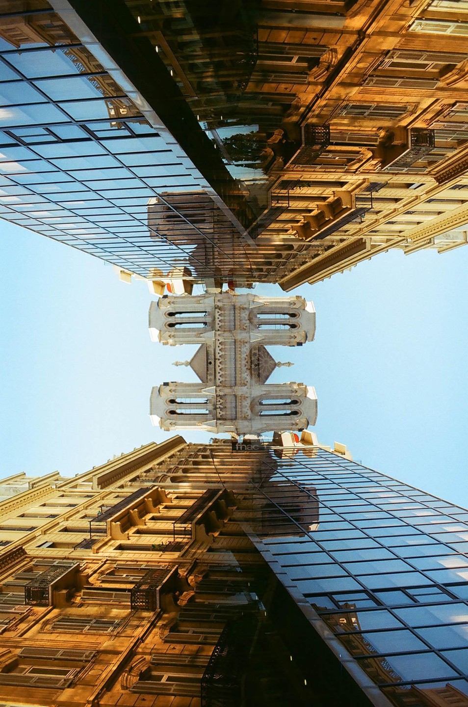 A double exposure shows a classical building and a modern glass building reflected in each other, with a clear blue sky in the background.