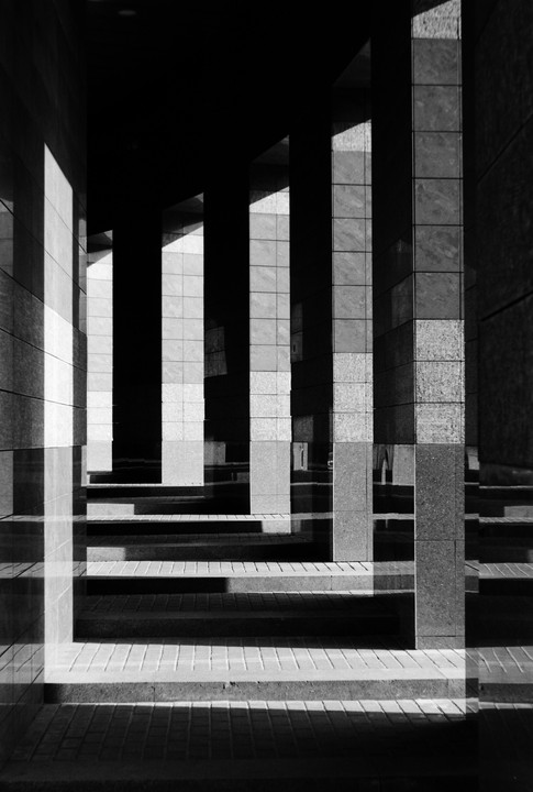 Sunlight casts strong shadows across a series of pillars and steps in a modern building.