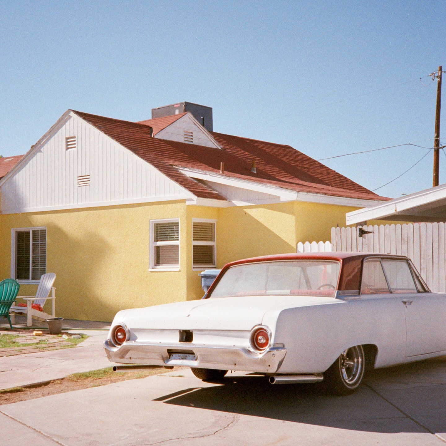 A white car with a red roof is parked in a driveway next to a yellow house with a red roof.