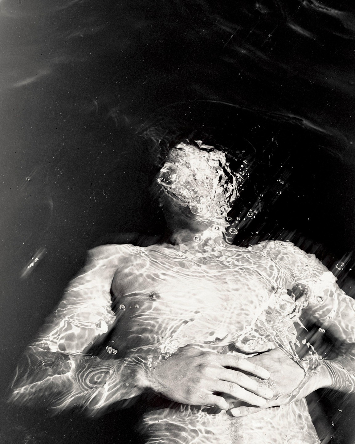 A man is submerged in water with his face partially obscured by bubbles and ripples.