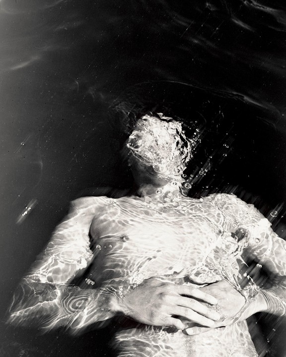 A man is submerged in water with his face partially obscured by bubbles and ripples.