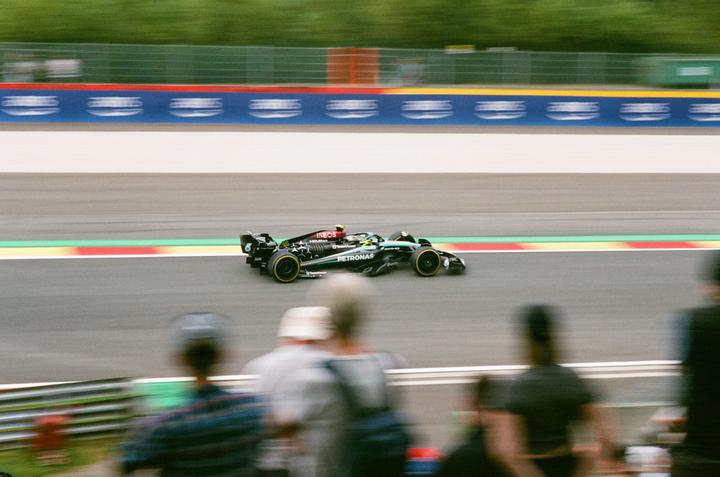 A black race car speeds along a track with spectators in the foreground.