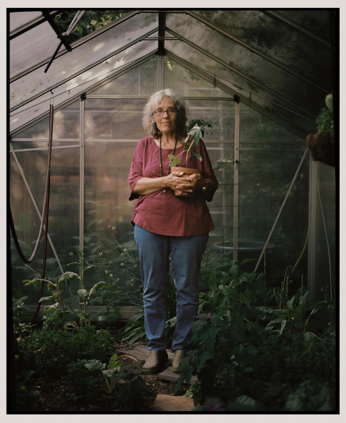 A woman stands in a greenhouse holding a potted plant.