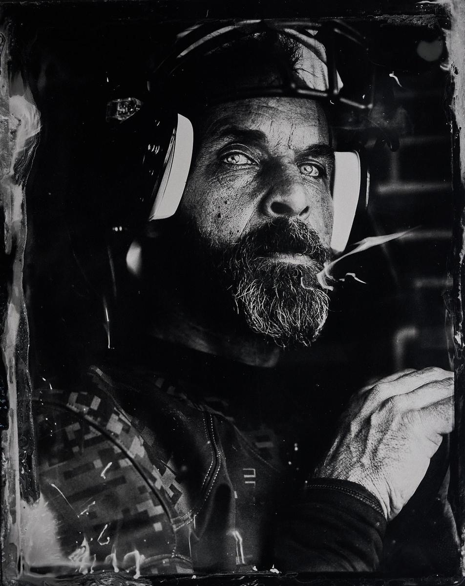 A man with a beard and headphones looks up, with smoke coming from his mouth.