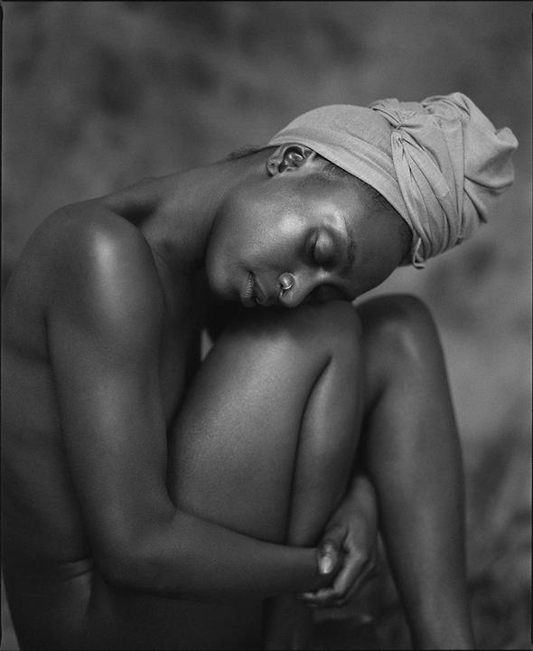 A woman with a head wrap is sitting with her eyes closed and her head resting on her knees.