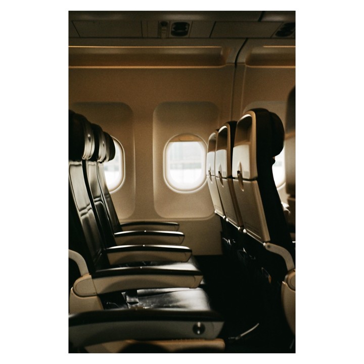 The interior of an airplane cabin shows rows of empty seats and windows.