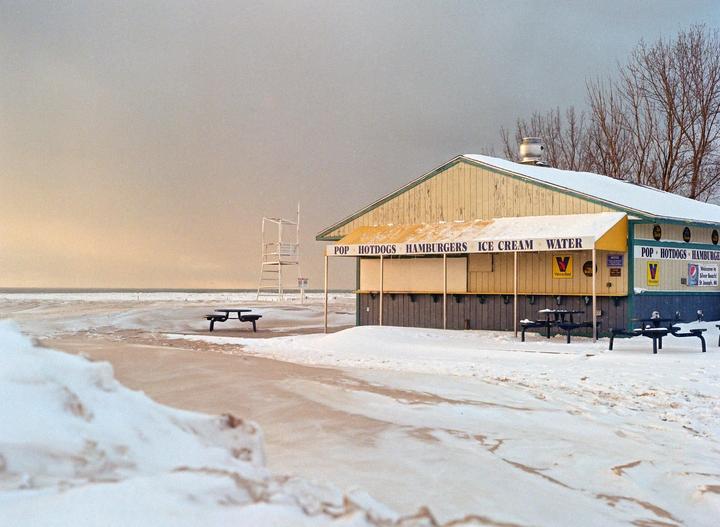 A snow-covered beach with a concession stand and a lifeguard chair under a cloudy sky.